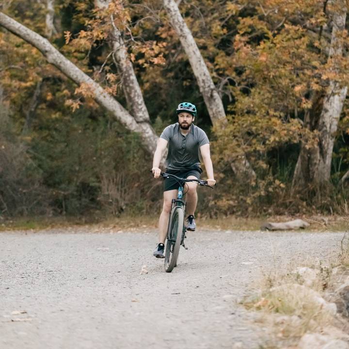 A cyclist rides on a gravel path surrounded by autumn trees, wearing a Rowan Mountain Bike Helmet and athletic clothing.