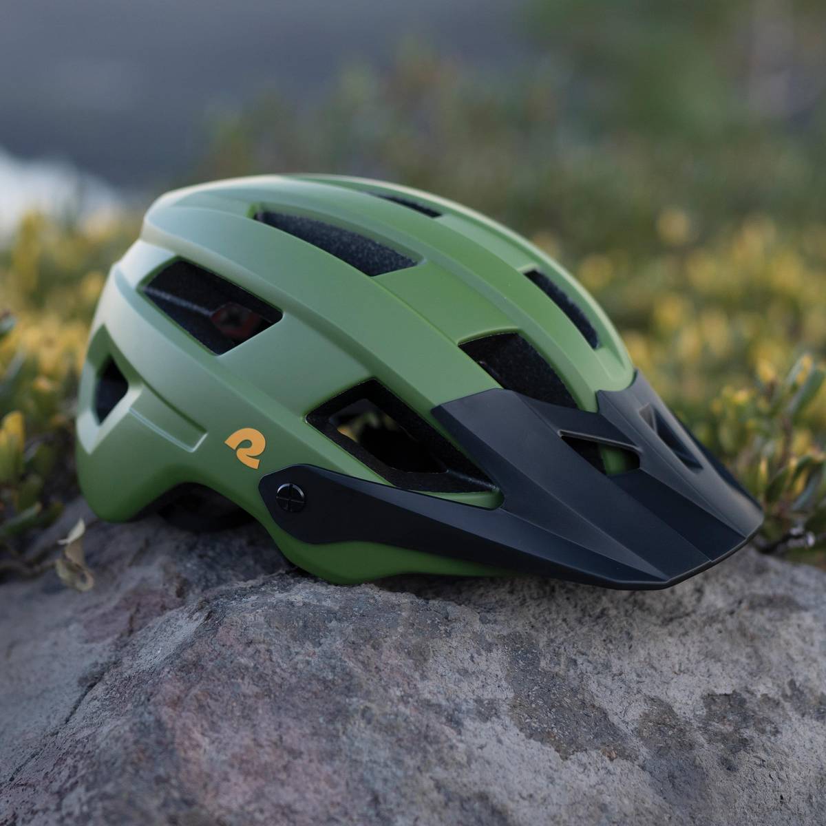 A green and black Rowan Mountain Bike Helmet rests on a rock, showcasing its modern design and ventilation features.