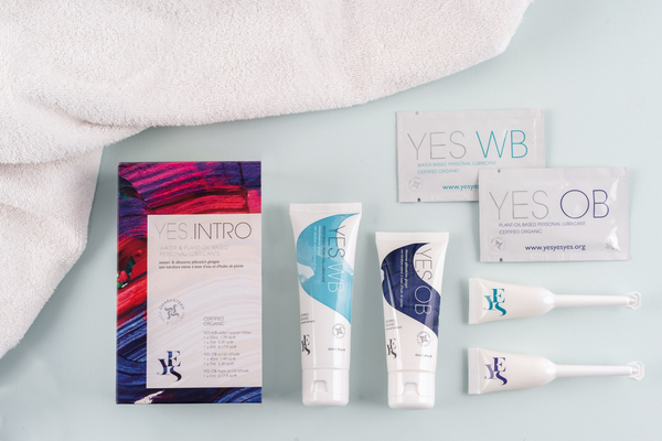 YES INTRO box with the contents spread out on a pale blue background with a white towel next to it.  Contents of the box are a tube of WB and OB next to an app of WB and OB, and a sachet of WB and OB
