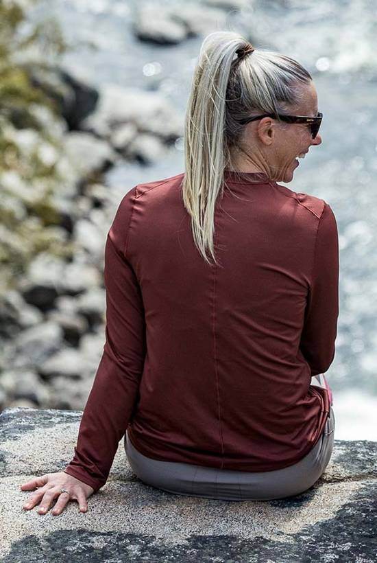 Woman wearing Mars Red Geo T viewed from the Back while sitting on a rock above a creek