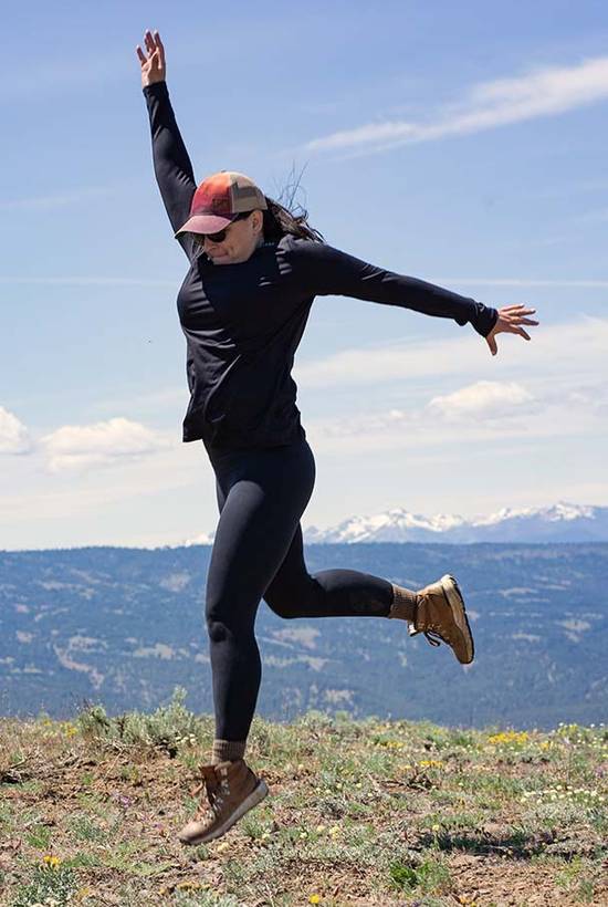 Woman wearing black Geo T Crew L.S Shirt jumping in the air on top of a mountain