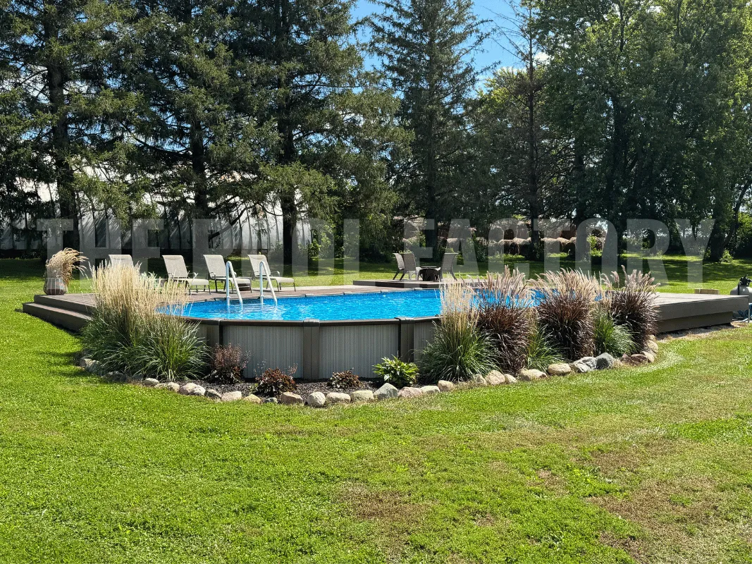 Oval above ground pool surrounded by beautiful landscaping and partial deck