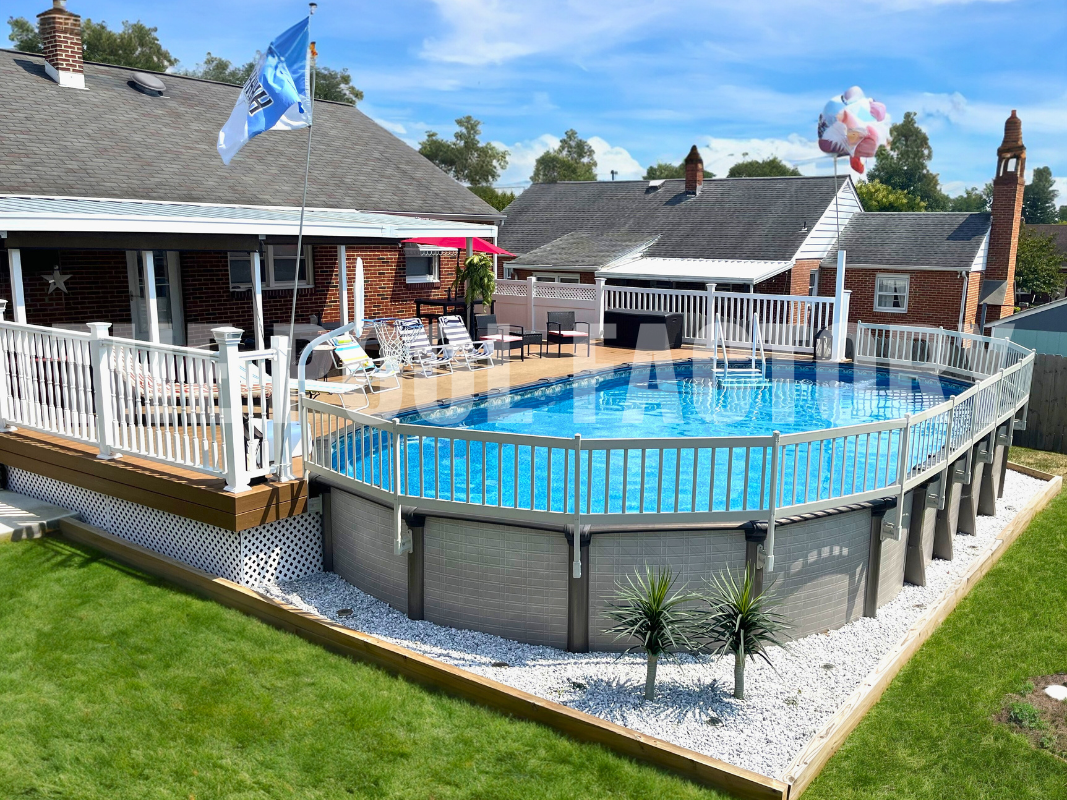 Oval above ground swimming pool with partial deck and fence surrounded by decorative rocks