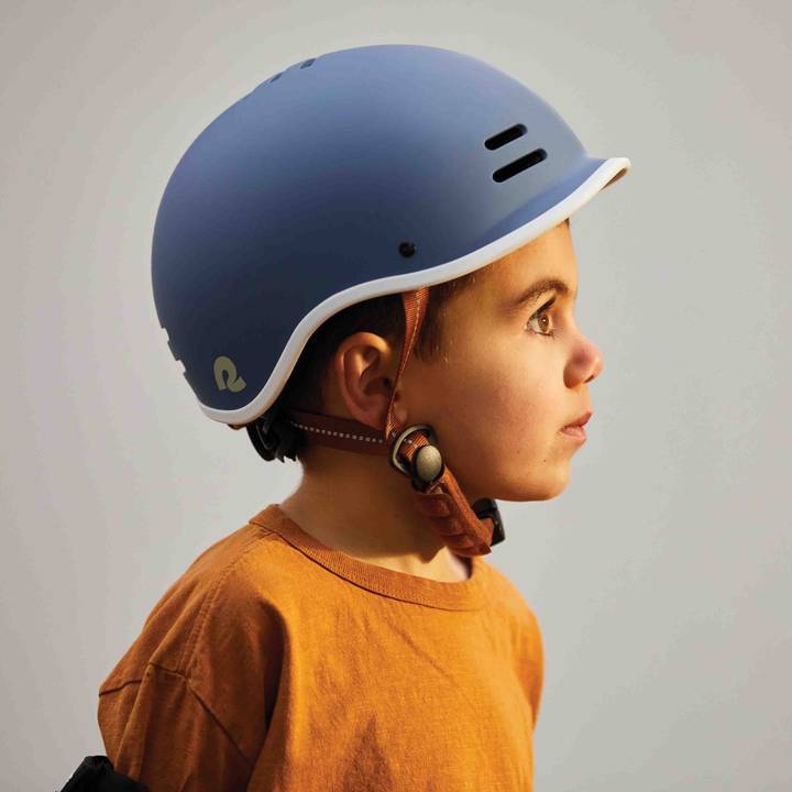 A young boy in a blue Remi Youth Bike & Skate Helmet gazes off to the side, looking thoughtful and adventurous.