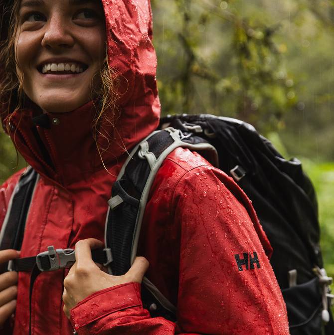 Up close of a women wearing a red rain jacket and backpack, with rain drops rolling off her jacket.