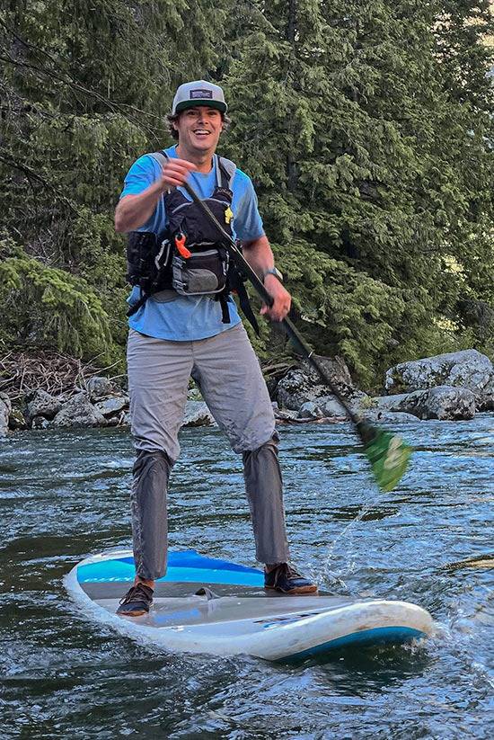 Man paddle boarding on a river with a lifejacket over the Solarswift Tech-T in Big Sky Blue and Tarngood Pants in Moonstone by Beyond Clothing.