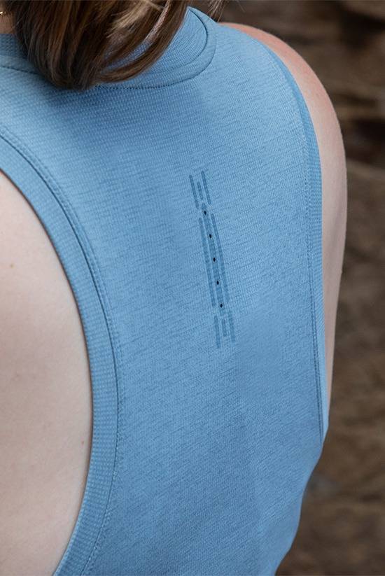 Close up photo of the upper back of a woman wearing the Feathers Tech-Tank in Big Sky Blue. Showcases the ventilation holes in the middle upper part of the tank top.