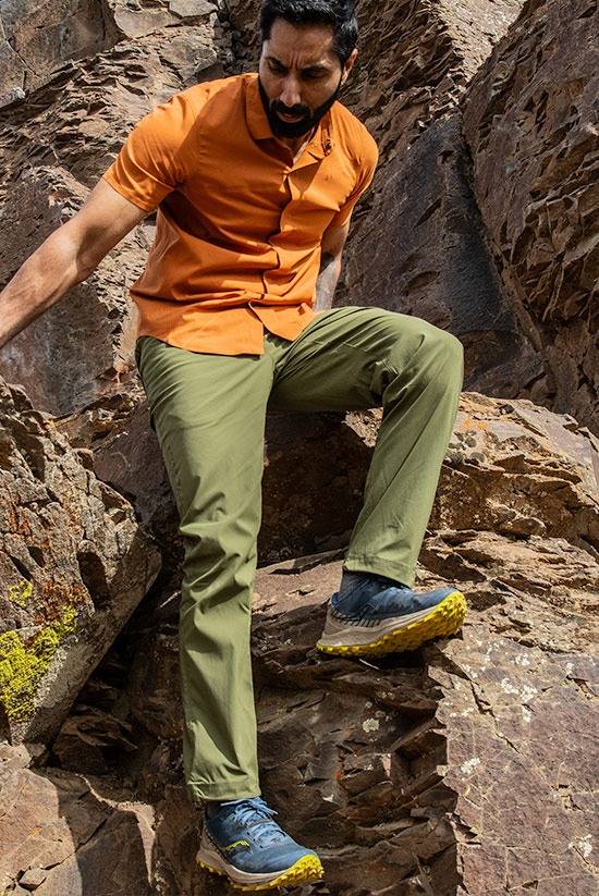 Man wearing the Evergreen TarnGood Pants while hiking down some rocks. Also wearing the Desert Clay FirstSun shirt.