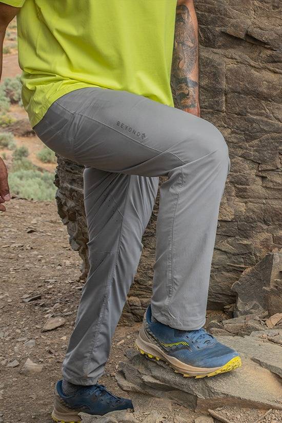 Man wearing the Moonstone colored TarnGood Pant with one leg up on a rock. Also wearing the light lime SolarSwift Tech-T.