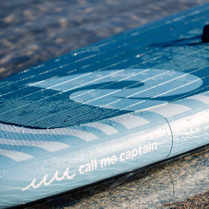 A close-up of the Great White Weekender Nano Inflatable Stand Up Paddle Board for kids with the phrase "call me captain" printed on its side, partially submerged in clear water.