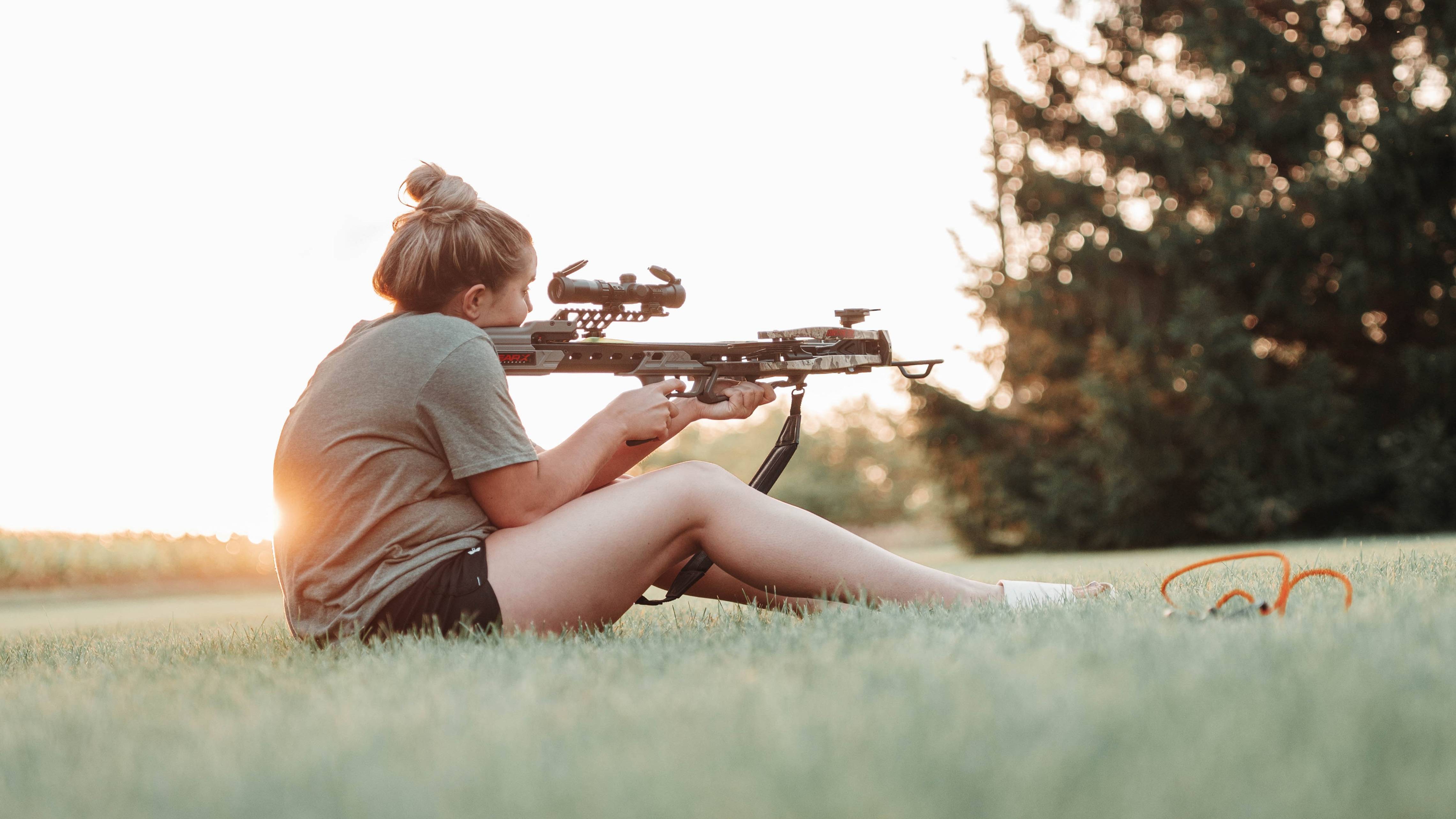 Woman sitting in the grass shooting a Bear Archery Constrictor Pro Hunting Crossbow