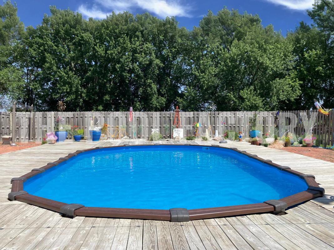 Oval semi inground swimming pool with a full wrap around deck, and fence surrounding property