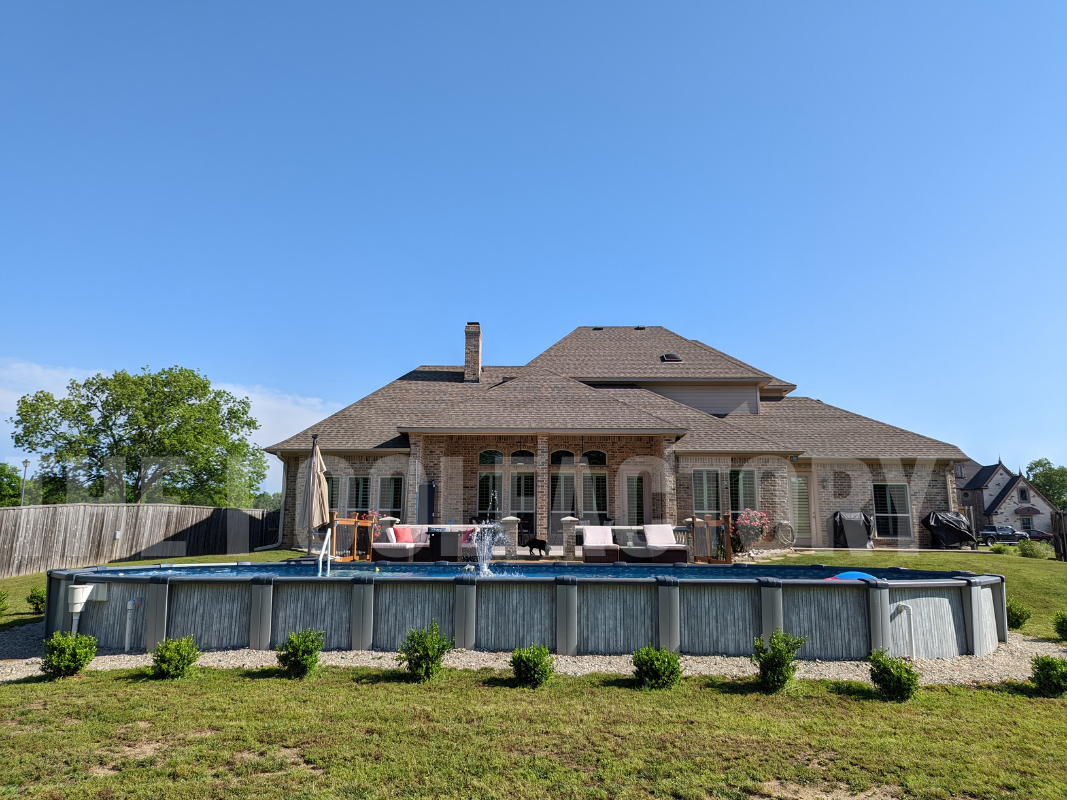 Oval above ground pool with deck, surrounded by green plants