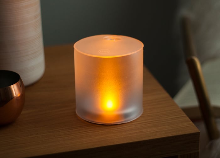 A frosted glass lamp emits a warm orange glow, placed on a wooden surface beside a metallic bowl.