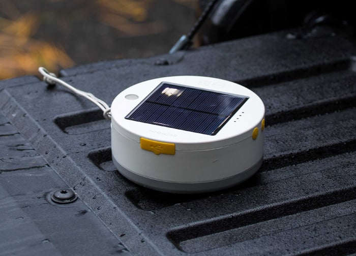 A round solar-powered light sits on a textured surface, featuring a solar panel and a yellow button.