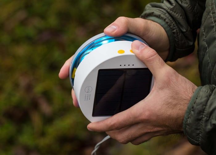 A person holds a round, solar-powered device with a blue and white design, featuring buttons and a solar panel on top.