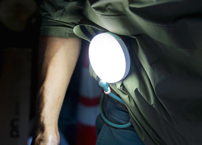 A person wearing a green shirt has a round, bright light attached to their side, illuminating the area around them.