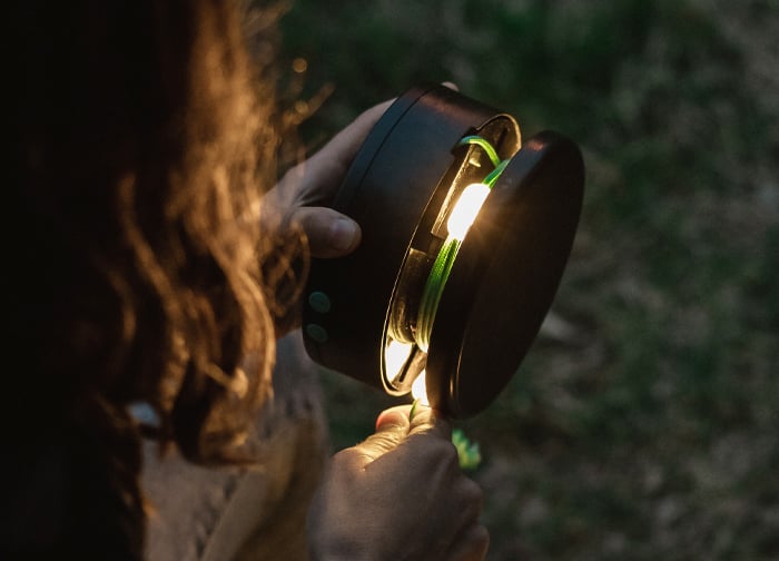 A person holds a compact lantern, illuminating a green cord inside, with a soft glow in a natural setting.
