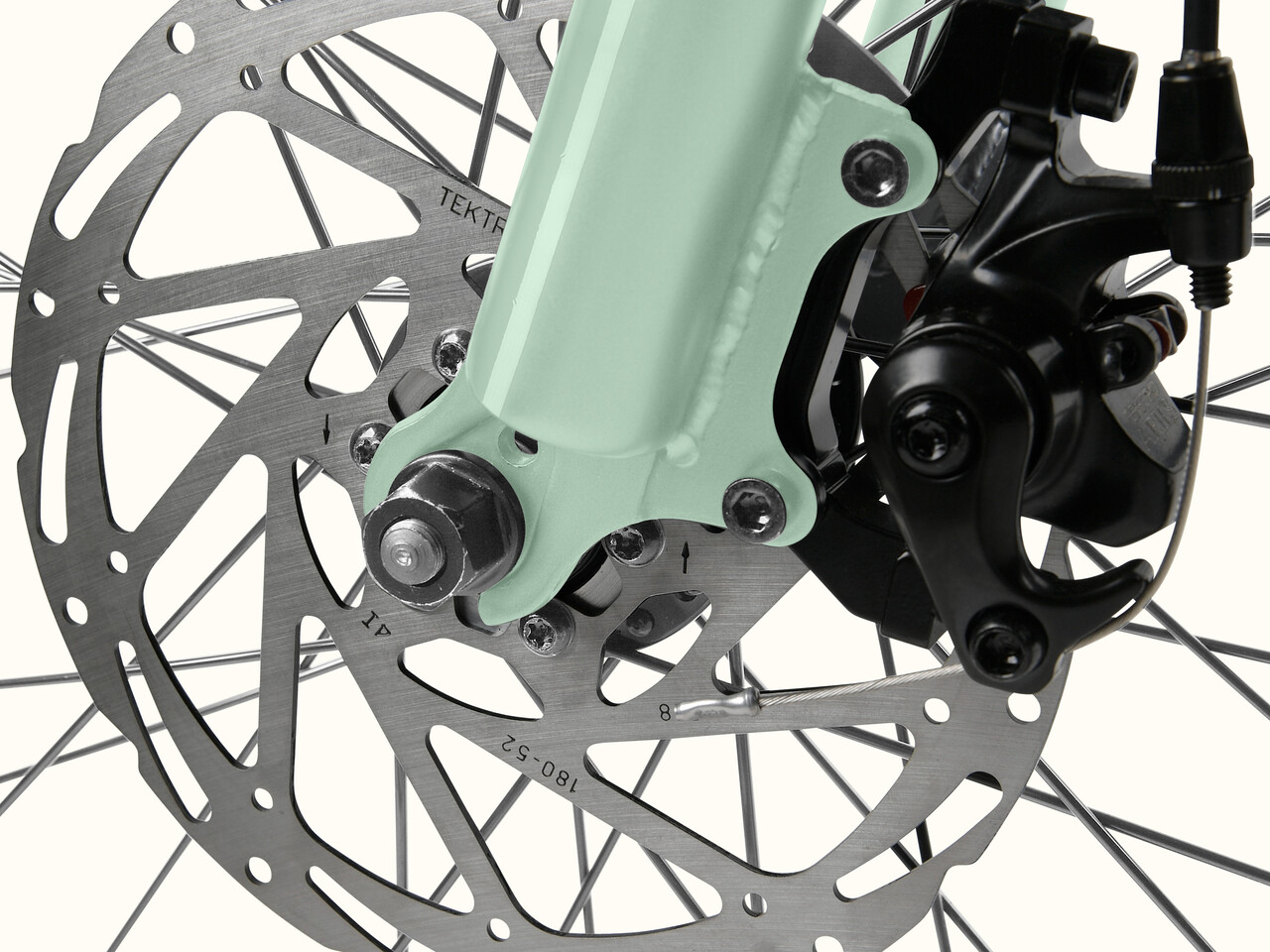 Close-up of the Chatham Rev+ 2 Beach Cruiser Electric Bike - Step Through's front disc brake, featuring a mint green fork, metallic rotor, and black caliper assembly.