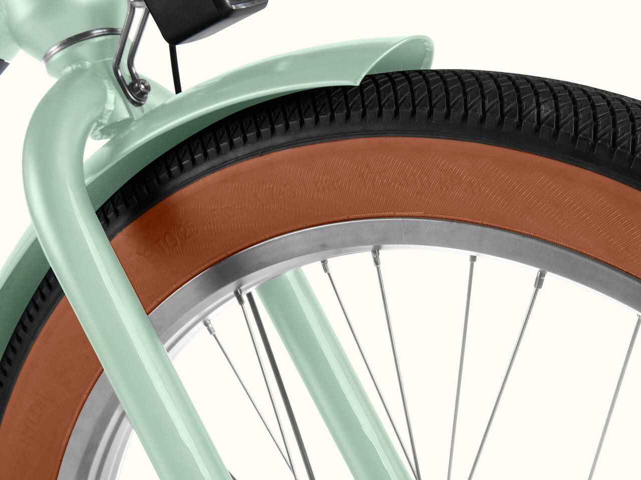 Close-up of a mint green Chatham Rev+ 2 Beach Cruiser Ebike's front wheel, featuring a textured brown tire and silver rim against a light background.