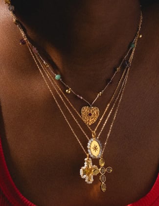 Four gold pendant necklaces close up layered on a neck