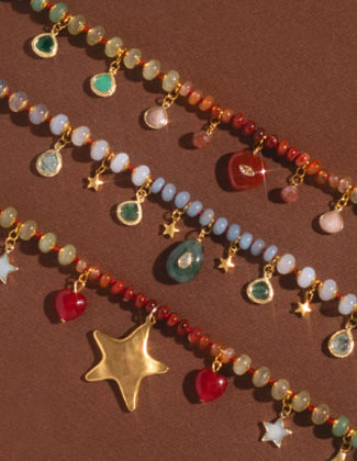 A close up of 3 colorful beaded charm necklaces laying on a warm brown background