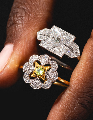 Two gold gemstone rings pinched between two fingers against a black background