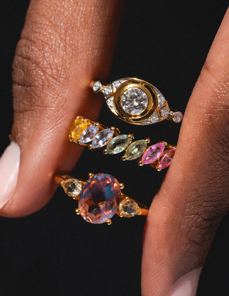 Close up of three gold gemstone rings pinched between two fingers