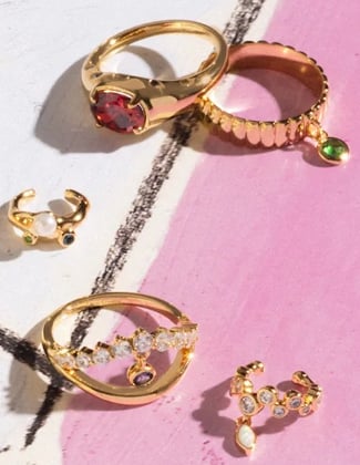Close up of gold rings and earrings laying on a pink and white background