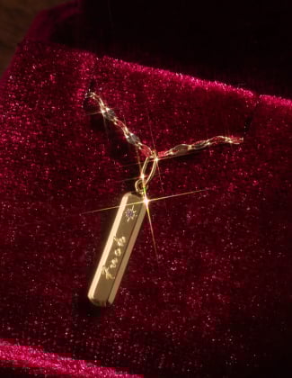 A close up of a gold charm engraved with the word fuck on a chain in a maroon velvet jewelry box