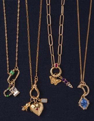 Close up of three gold charm necklaces laying on a black background