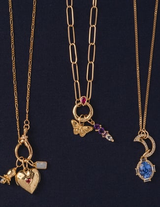 Close up of three gold charm necklaces laying on a black background