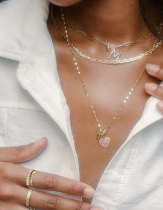 Close up of a woman wearing several pieces of gold jewelry including necklaces and rings in white collared shirt