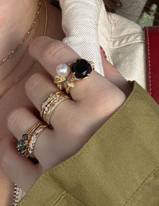 Close up of a hand with a green sleeve wearing several gold rings with gemstones stacked