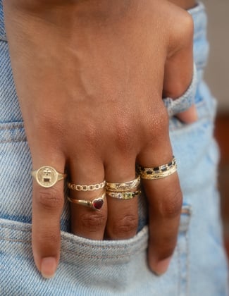 Close up of a woman's hand in a jean pocket wearing 7 gold rings stacked