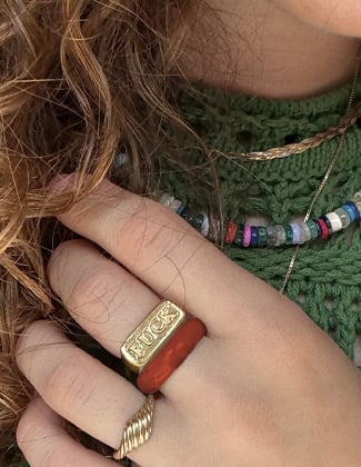 A close up selfie of a hand with three gold and stone rings in front of a green sweater