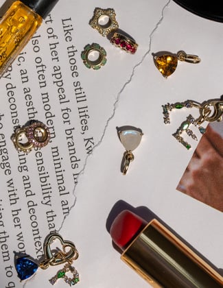 An assortment of gold charms laying on pieces of paper with a lipstick and perfume