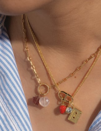 Close up of three gold charm necklaces layered on a neck with a blue and white striped shirt