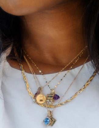 A close up of a woman in a white t-shirt wearing 4 layered solid gold necklaces with gemstone charms