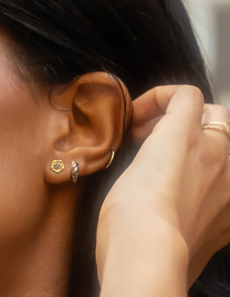 Six gold earrings- huggie hoops, studs and cuffs- on a slice of orange hold by a hand against a cloud background