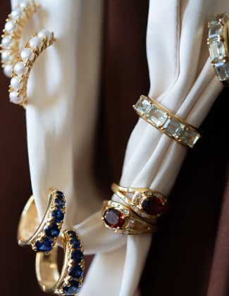 4 pairs of gold gemstone earrings hanging on cream satin