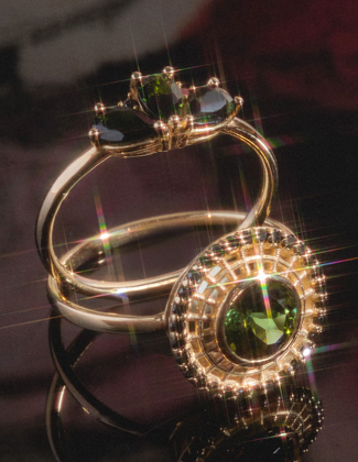 Two gold rings with dark gemstones laying against a dark background