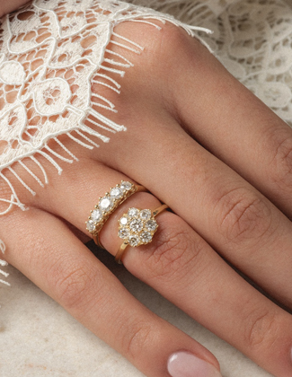 A close up of a hand with a white lace sleeve wearing gold wedding ring stack