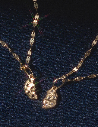 A close up of two diamond studded gold charms on gold chhains laying on a dark blue background