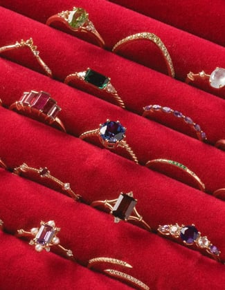 A close up of several gold gemstone rings in a red velvet ring tray