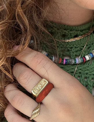 A close up selfie of a hand with three gold and stone rings in front of a green sweater