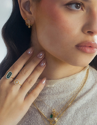 Close up of woman's face and hand wearing assorted gold and gemstone jewelry