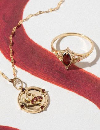 Gold garnet ring and necklace laying on a painted surface