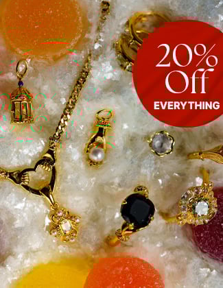 An assortment of gold gemstone jewelry laying in faux snow with a red badge that reads 20% off everything