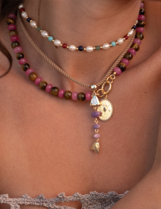 A close up of a neck wearing gold and beaded chains with gemstone and gold charms
